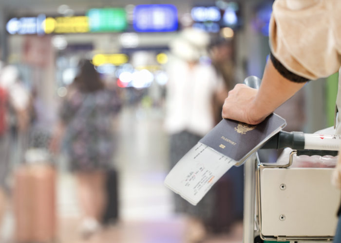 Close up of woman holding a boarding pass and passport while pushing a cart through an airport