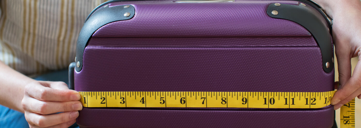 Close up of woman measuring a purple carry on suitcase with a yellow measuring tape