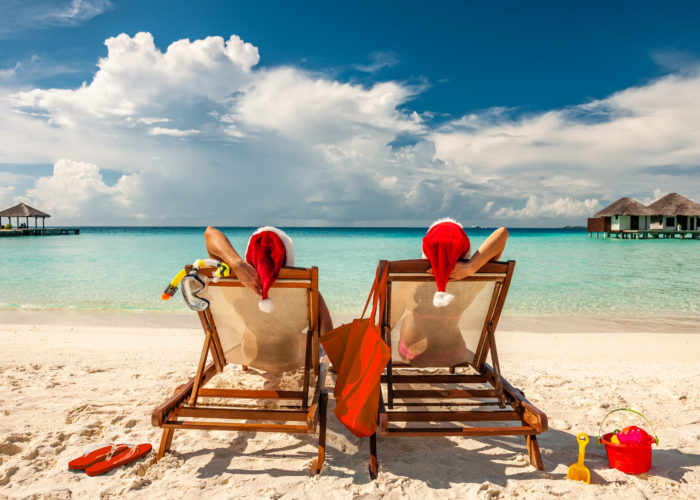 Couple sitting on lounge chairs on the beach in Santa hats