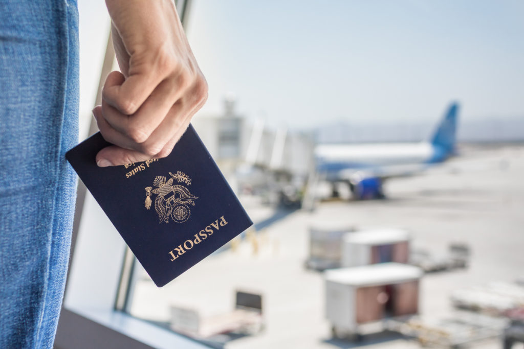 Close up of hand holding a US Passport in front of a window in an airport looking out over planes on the tarmac