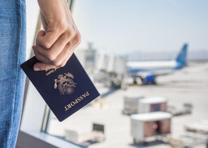 Close up of hand holding UC passport in front of airport window showing airplane on runway