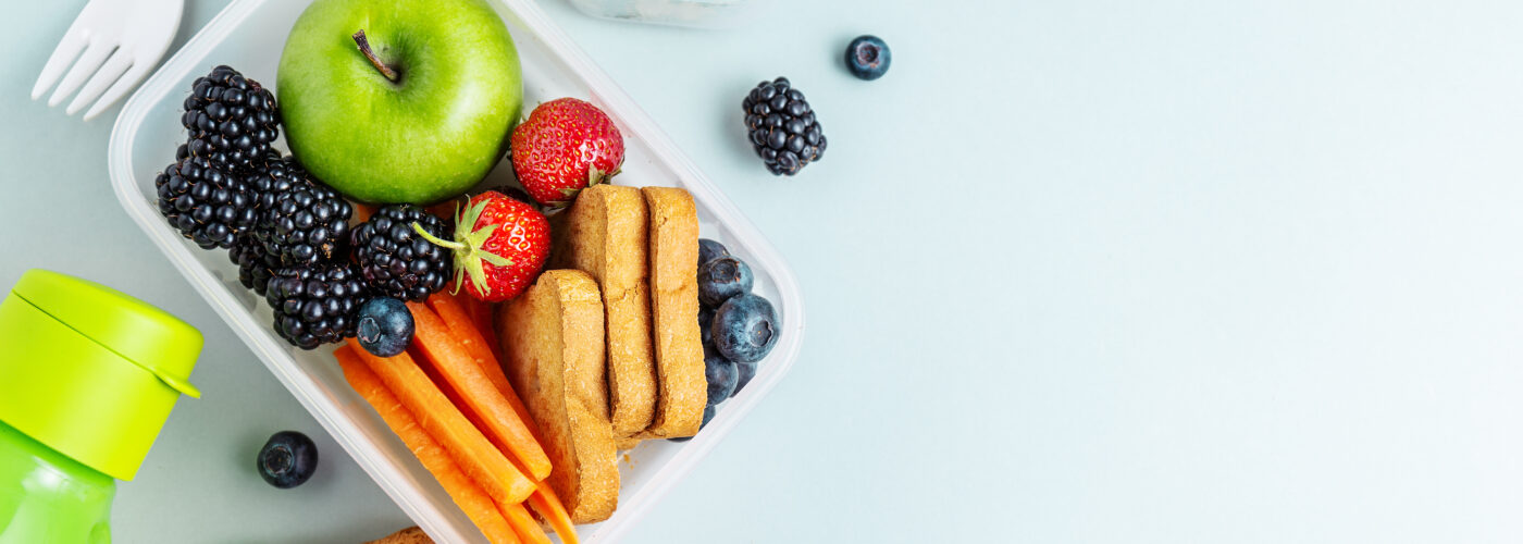 Overhead view of a packed lunch full of fruits and vegetables on a pale blue table