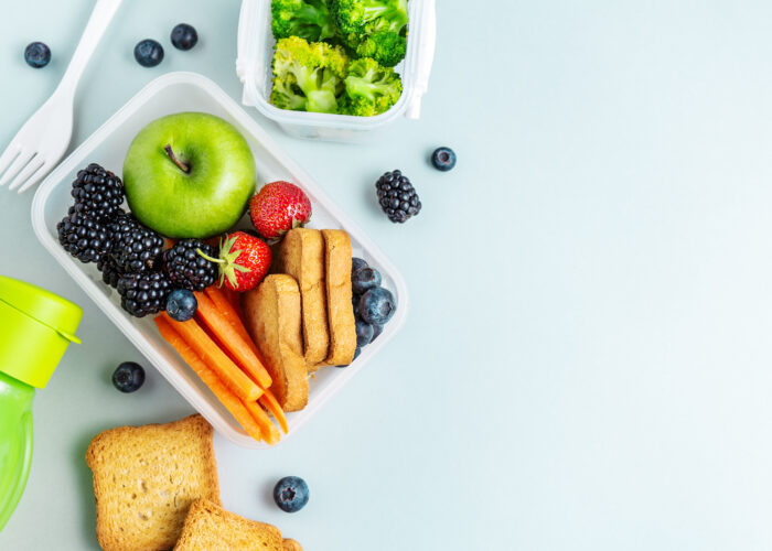 Overhead view of a packed lunch full of fruits and vegetables on a pale blue table