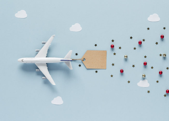 A toy plane on a blue backdrop attached to a tag with small Christmas ornaments trailing behind it