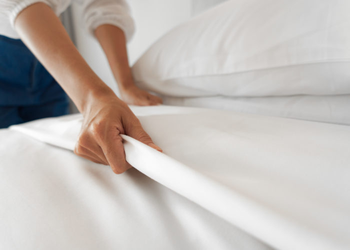 Close up of hand making hotel bed with white sheets