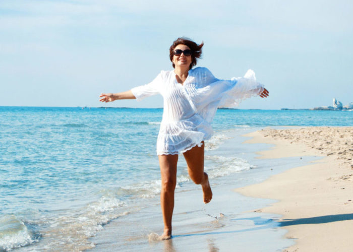 Woman running toward camera on beach in white beach cover up