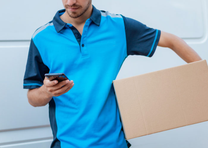 Close up of a man in a blue shirt reading on his phone while delivering a package