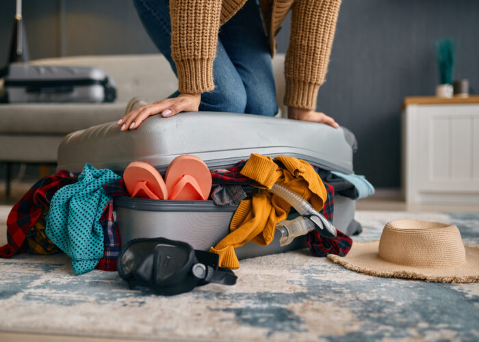 Close up of person pressing down top of overfull suitcase