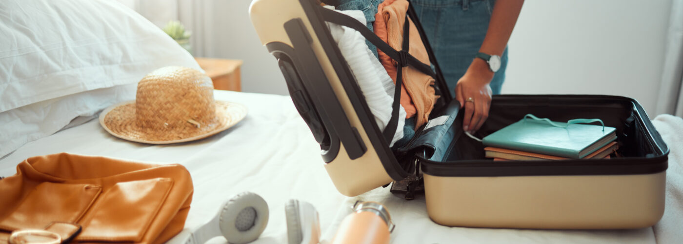 Person packing a hardside suitcase with travel gear on their bed