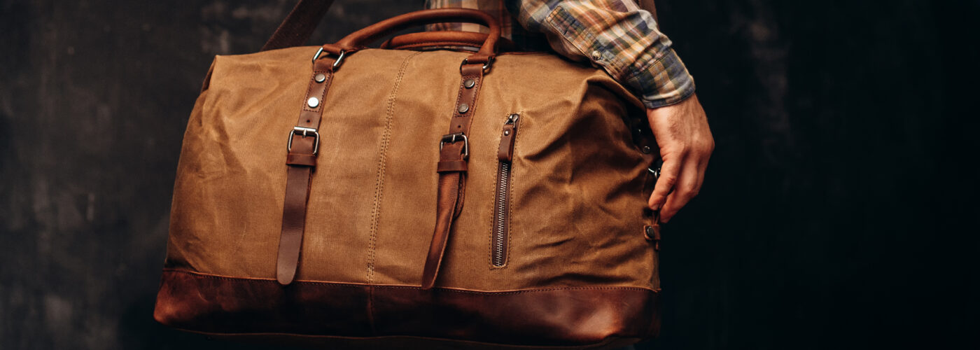 Close up of man holding a brown leather duffel bag