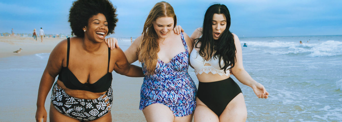 Three women walking through waves at the beach and laughing