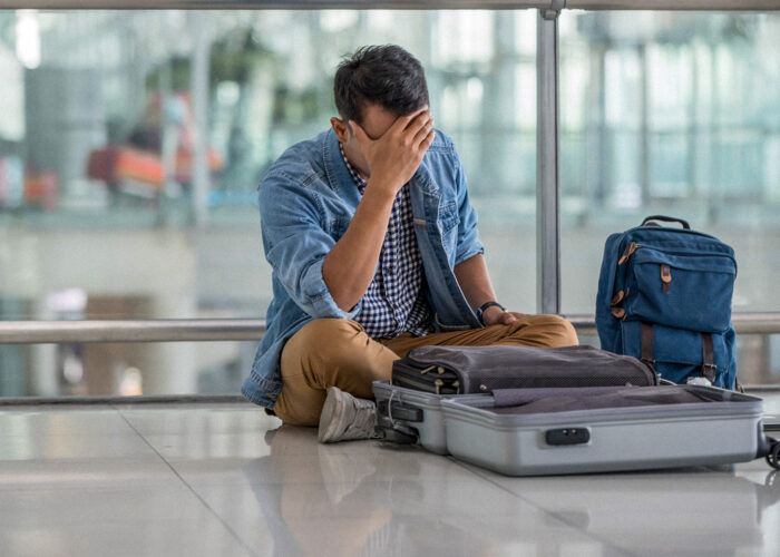 man sitting on floor at airport with open luggage lost item