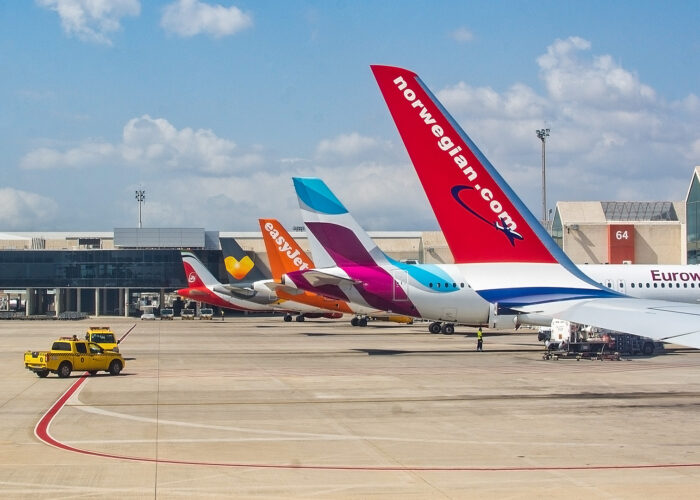 planes parked at airport in a row. Airplane tail fins from Norwegian, Eurowings, Easyjet on the tarmac