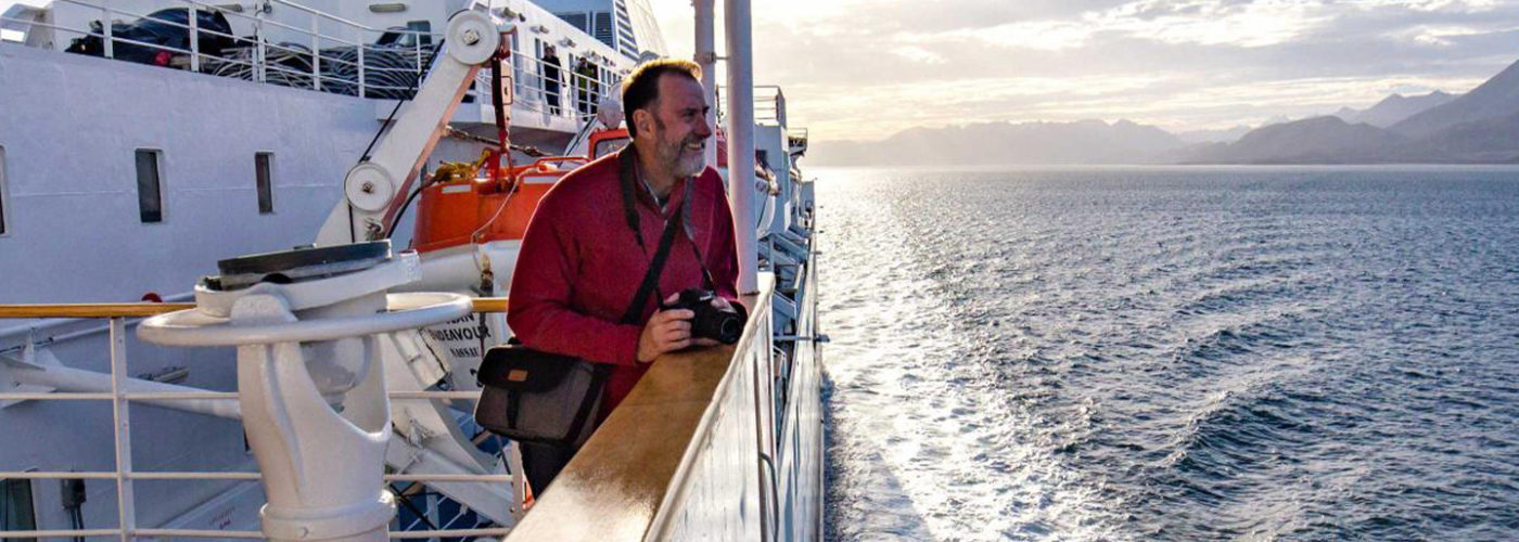 Man holds camera, leaning over railing of ship in Antarctica